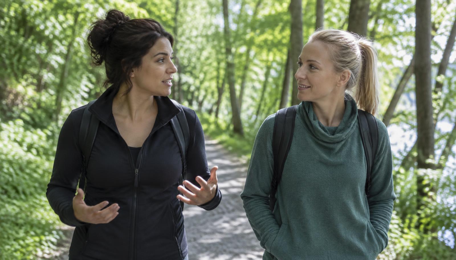 Two women walking and talking on a sunlit trail
